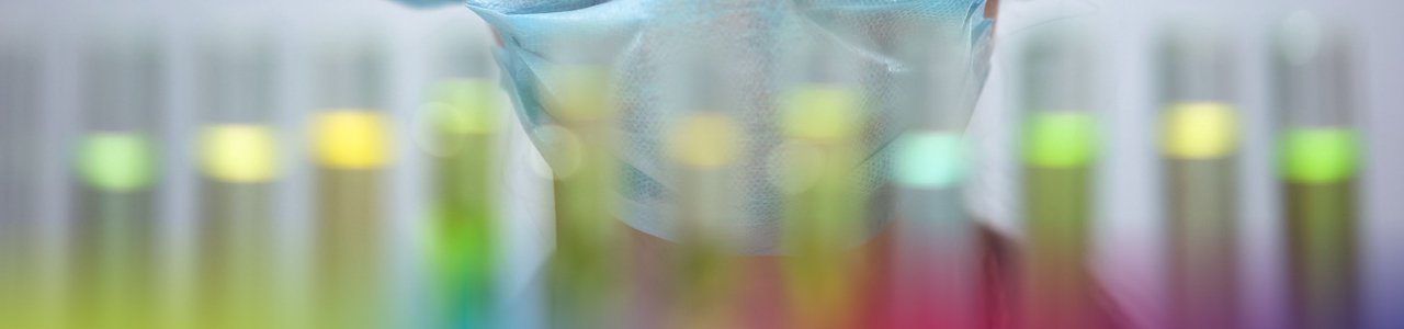Chemiker mit Schutzbrille auf und Reagenzgläser vor sich