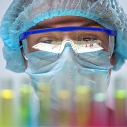 Chemiker mit Schutzbrille auf und Reagenzgläser vor sich